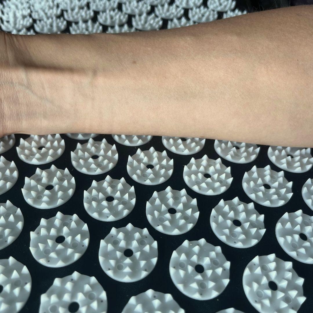An arm on top of an acupressure mat with multiple mini spikes.