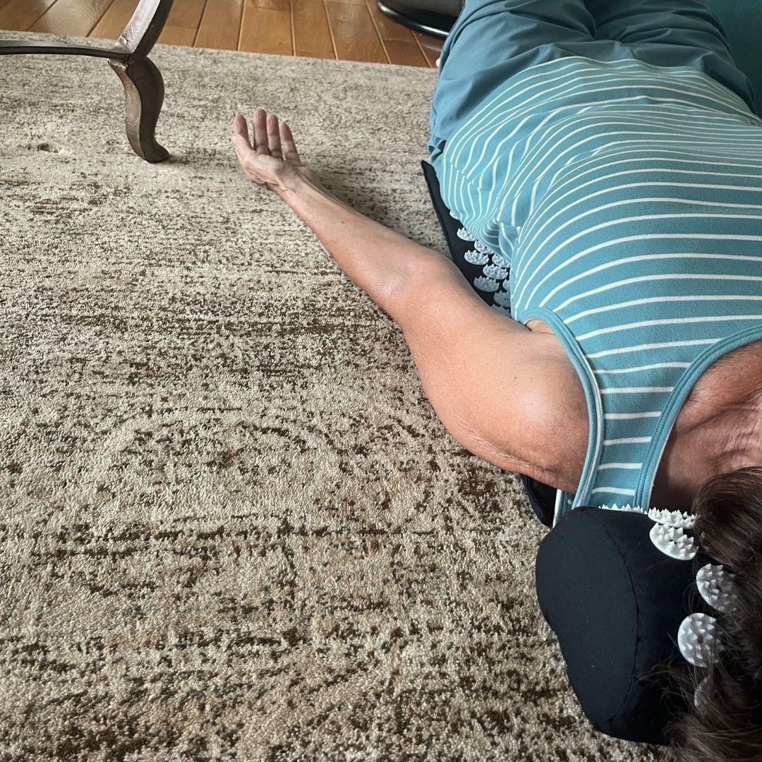 An over the shoulder angle shot of someone lying down on an acupressure mat on the floor.